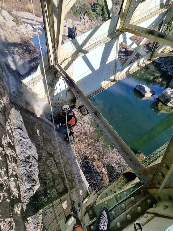 Cordiste suspendu sous le tablier métallique d'un pont, au-dessus de l'eau