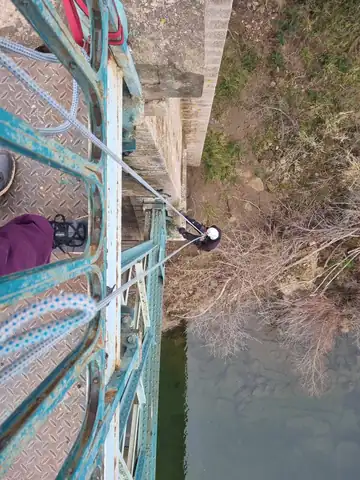 Cordiste en descente le long d'un pont métallique, au-dessus de la rivière